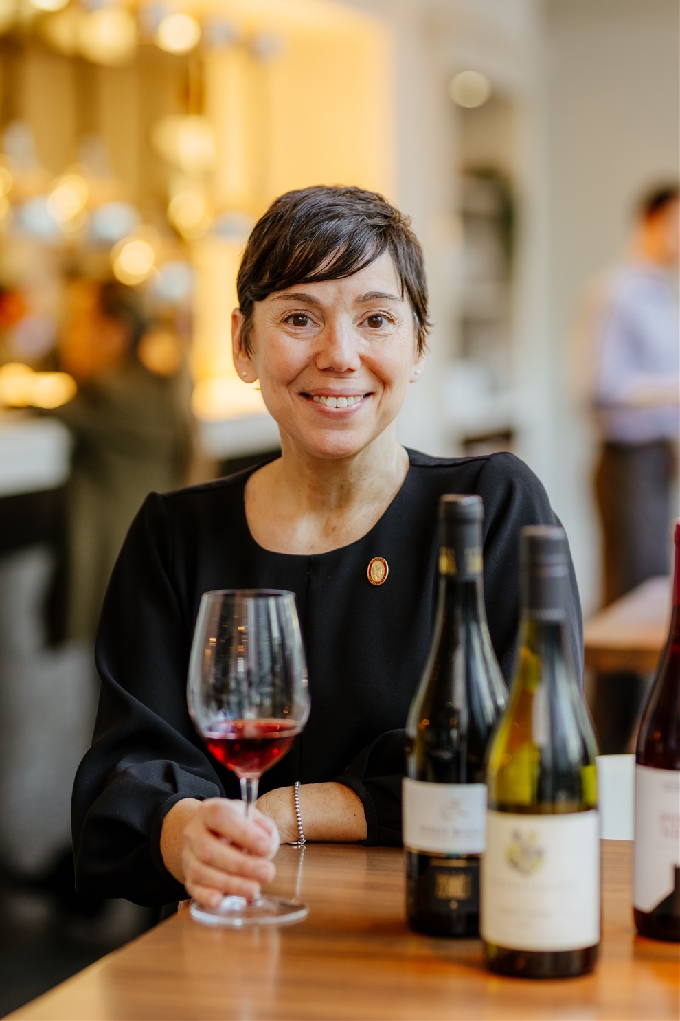 Woman in black dress drinking wine and smiling at the camera